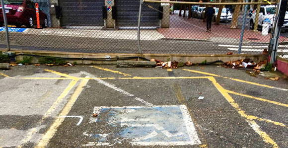 A poorly maintained parking lot. The disability parking symbol is faded and trash is strewn about.