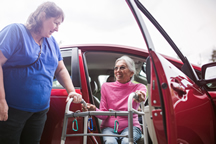 Woman will a walker being helped out of a car