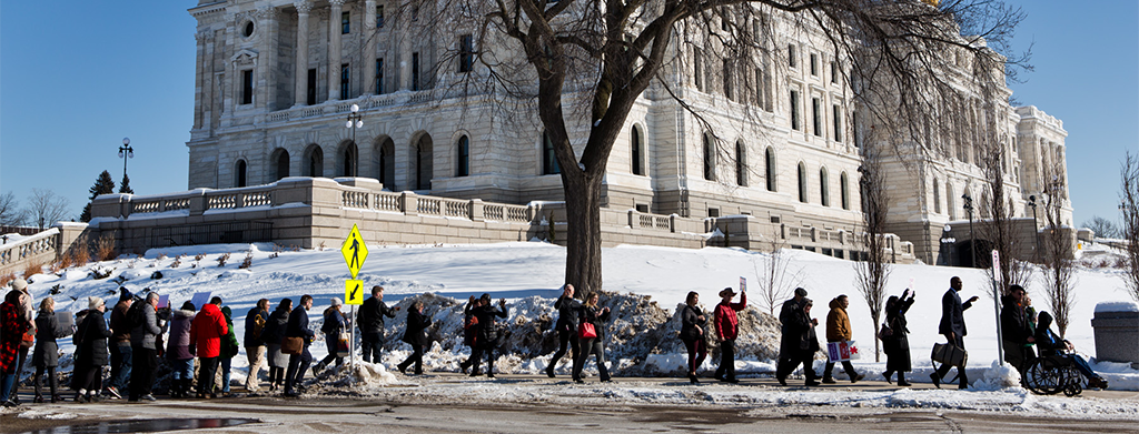 Members of the disability community marching and rolling together on the State Capitol sidewalk