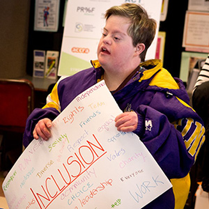 Disability advocate holding a poster. The most prominent word, among a group of such, is Inclusion.