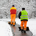 Two people in high visibility clothing clearing snow off a path
