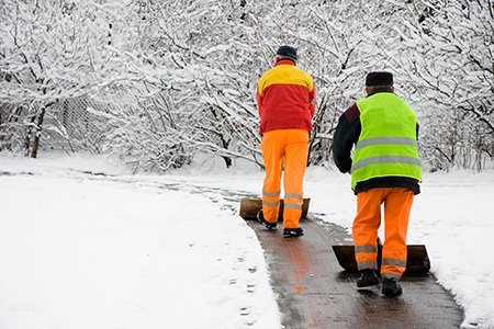 Two people in high visibility clothing clearing snow off a path