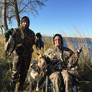 Hunter in a wheelchair poses with ducks and a hunting dog