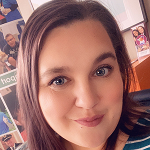 Jillian wearing a blue and white blouse. She has brown hair and is smiling.