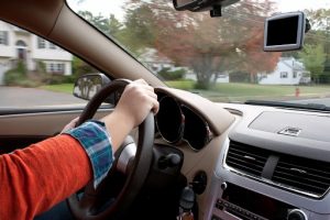 A woman holds the steering wheel of a car while driving down the road.