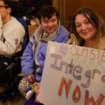 Attendees at the 2023 Disability Advocacy Rally. One holds a sign reading #Olmstead Integration Now! (partially cut off in photo)