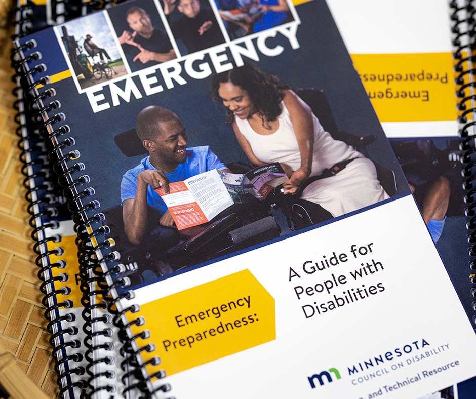A pile of emergency preparedness guides laying in a basket. The cover features photos of people with disabilities, including two people in wheelchairs looking at the guide together. Text reads: "Emergency Preparedness: A Guide for People with Disabilities. Minnesota Council on Disability."