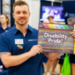 Public Policy Director Trevor Turner holds a poster with the text "Disability Pride!" Behind that are words associated with disability pride, including "supported," "inclusion," and "independence."