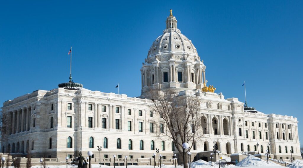 The Minnesota State Capitol building on a sunny winter day. Snow covers the ground, and flags fly on the roof.