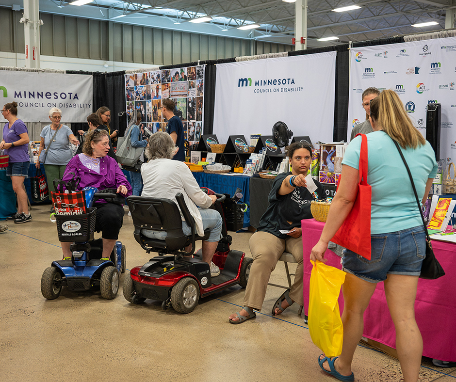 Fairgoers, including two people using mobility scooters, visit MCD’s Minnesota State Fair booth.